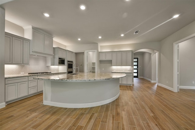 16146 Rustling Woods Rd, Conroe, TX 77302 - kitchen with gray cabinets, arched walkways, a spacious island, decorative backsplash, and light wood finished floors