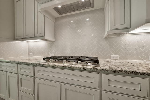 16146 Rustling Woods Rd, Conroe, TX 77302 - kitchen with wall chimney range hood, stainless steel gas cooktop, backsplash, and light stone counters