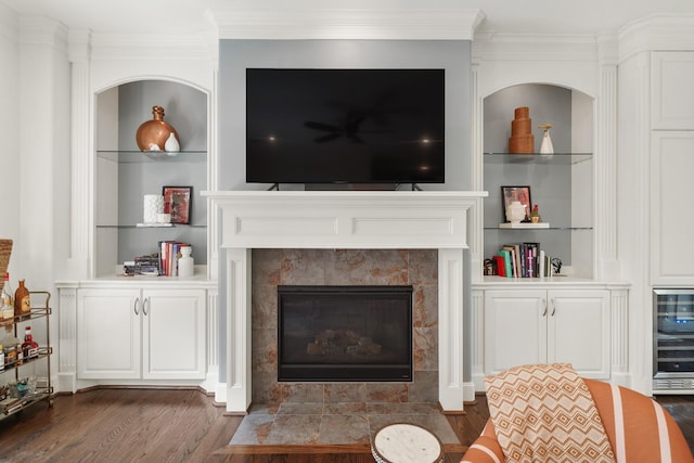 living room with built in shelves, ornamental molding, wine cooler, and a tiled fireplace