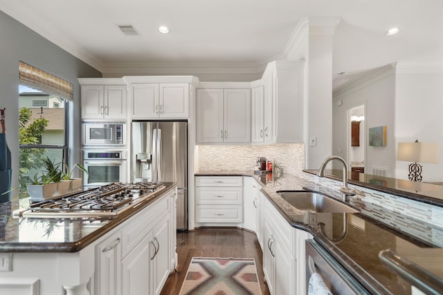 kitchen with appliances with stainless steel finishes, dark hardwood / wood-style flooring, dark stone counters, sink, and white cabinetry