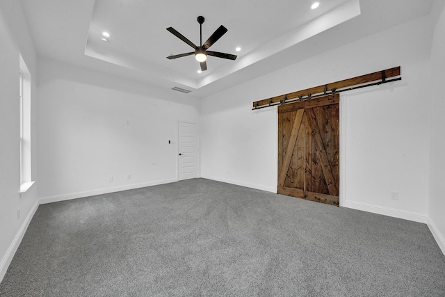 unfurnished room featuring dark carpet, a barn door, a raised ceiling, and ceiling fan