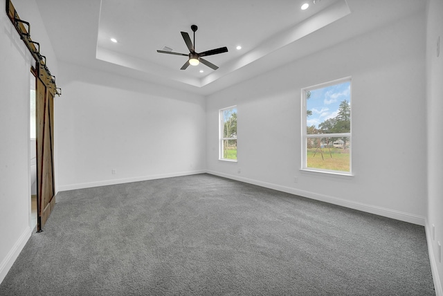 spare room with a raised ceiling, a barn door, ceiling fan, and carpet