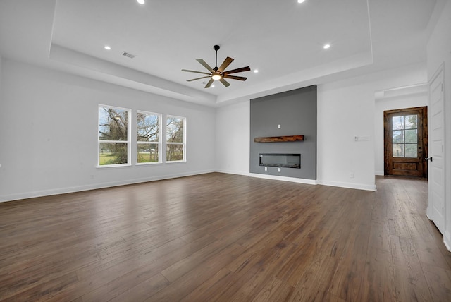 unfurnished living room with a raised ceiling, ceiling fan, and dark hardwood / wood-style floors