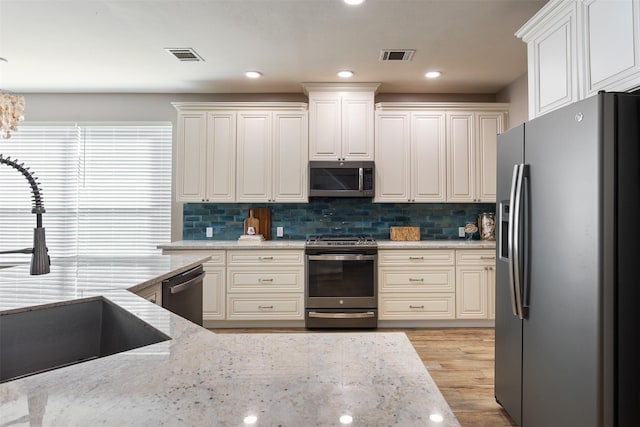 kitchen featuring light stone counters, sink, stainless steel appliances, and light hardwood / wood-style floors