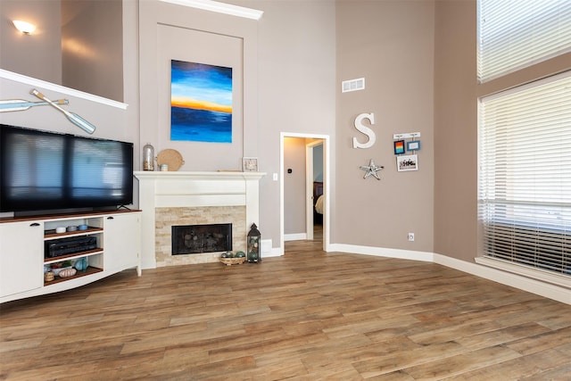 unfurnished living room with hardwood / wood-style floors, a towering ceiling, and a tiled fireplace