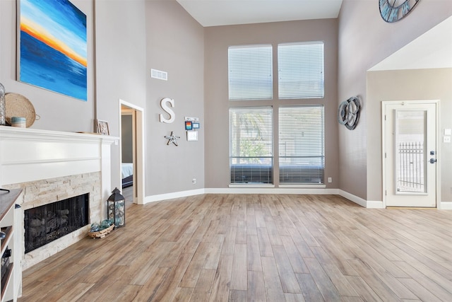 living room with a high ceiling, light hardwood / wood-style flooring, and a stone fireplace