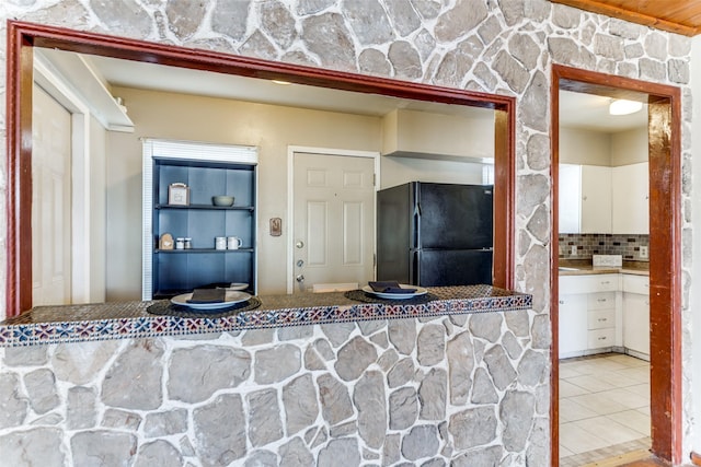 interior space featuring light tile patterned flooring, black fridge, white cabinetry, and tasteful backsplash