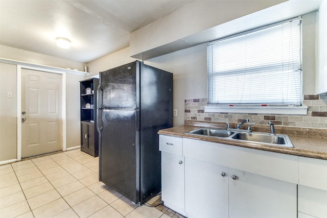 kitchen with white cabinets, black fridge, sink, light tile patterned floors, and tasteful backsplash