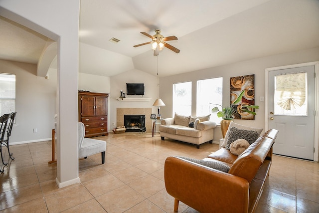 living area featuring visible vents, a tiled fireplace, a ceiling fan, vaulted ceiling, and baseboards