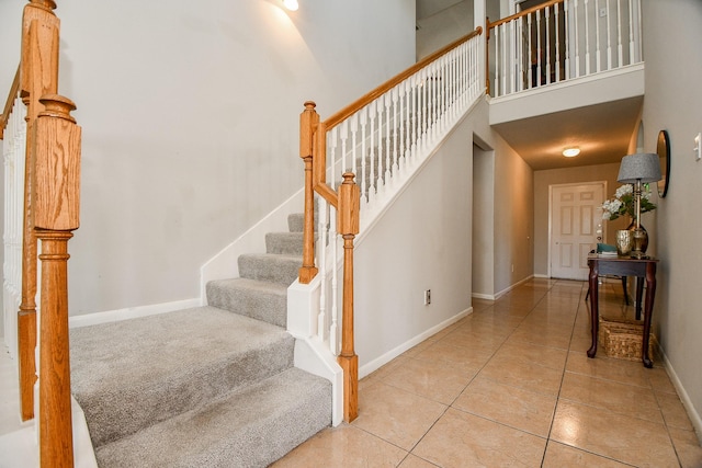 staircase featuring tile patterned flooring, a towering ceiling, and baseboards