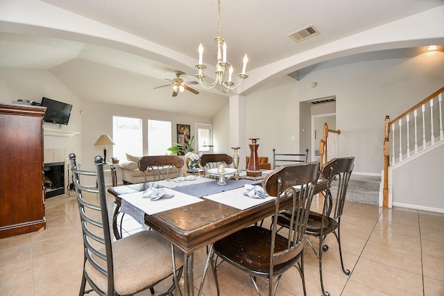 dining space with lofted ceiling, a tile fireplace, ceiling fan with notable chandelier, visible vents, and stairway