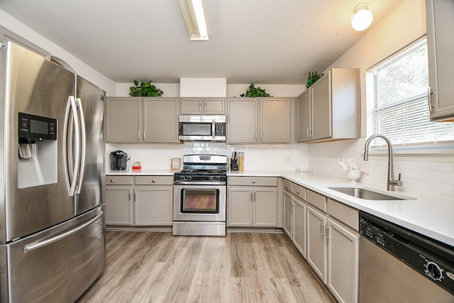 kitchen featuring tasteful backsplash, stainless steel appliances, light countertops, light wood-type flooring, and a sink