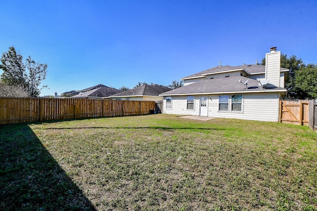 rear view of property featuring a fenced backyard, a chimney, a gate, a yard, and a patio area