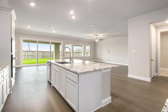 kitchen with light stone counters, sink, white cabinets, and a center island with sink