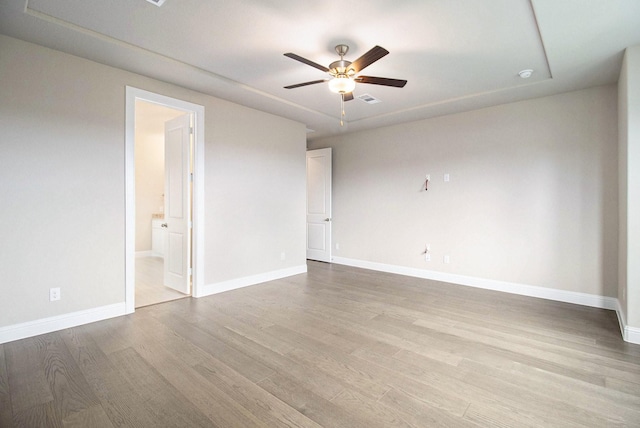 spare room featuring a tray ceiling, ceiling fan, and light wood-type flooring