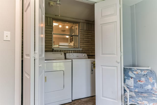 laundry room with dark hardwood / wood-style flooring, washing machine and dryer, and brick wall