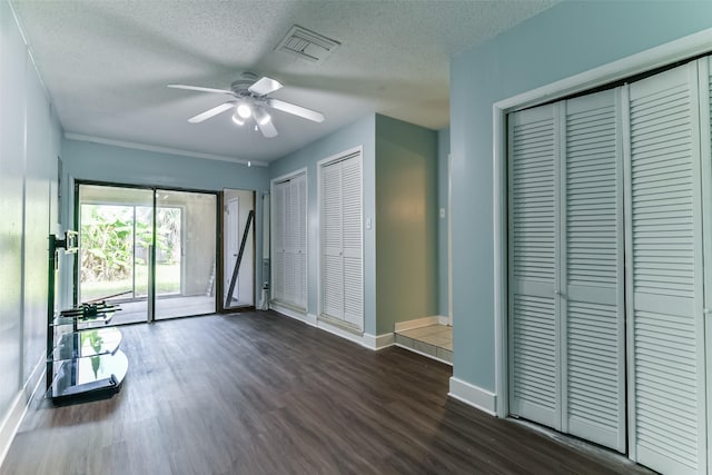 unfurnished bedroom featuring a textured ceiling, dark wood-type flooring, ceiling fan, and multiple closets