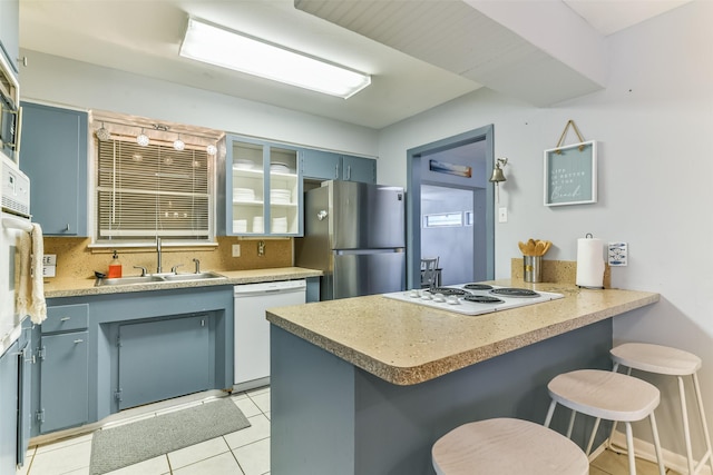 kitchen with a breakfast bar, white appliances, blue cabinets, sink, and kitchen peninsula