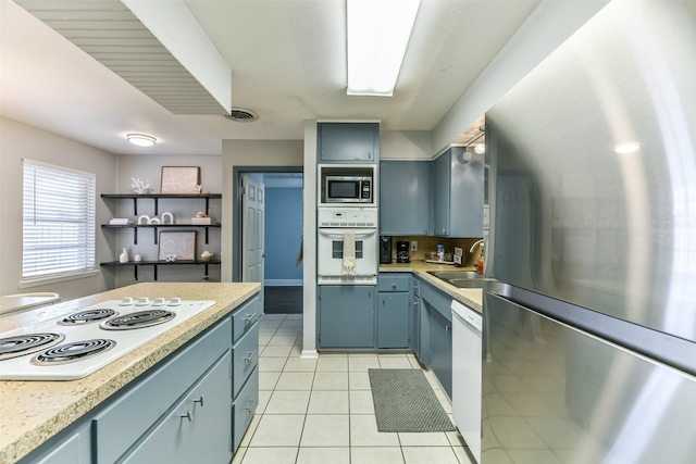 kitchen featuring blue cabinetry, light tile patterned floors, sink, and appliances with stainless steel finishes