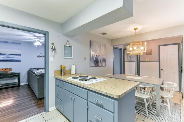 kitchen featuring kitchen peninsula, white electric cooktop, pendant lighting, light tile patterned floors, and ceiling fan with notable chandelier