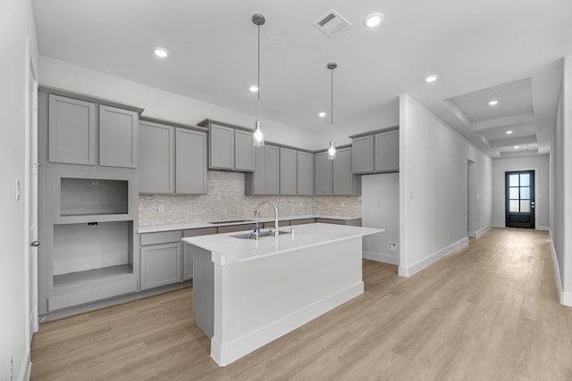 kitchen featuring gray cabinetry, pendant lighting, sink, an island with sink, and light hardwood / wood-style floors