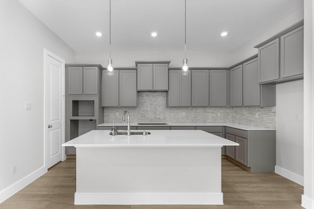 kitchen with gray cabinetry, sink, wood-type flooring, pendant lighting, and an island with sink