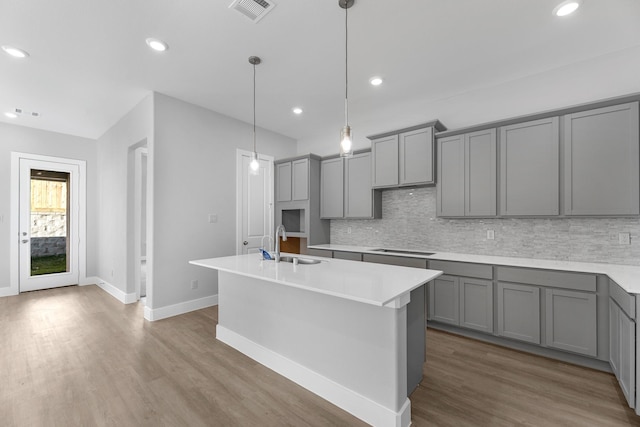 kitchen featuring gray cabinetry, sink, tasteful backsplash, pendant lighting, and a center island with sink