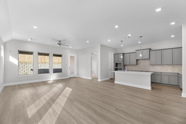 kitchen featuring light wood-type flooring, gray cabinetry, ceiling fan, decorative light fixtures, and an island with sink