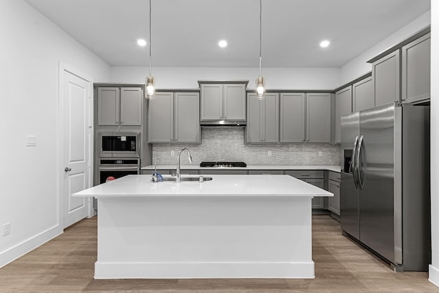 kitchen with appliances with stainless steel finishes, gray cabinets, pendant lighting, and a center island with sink