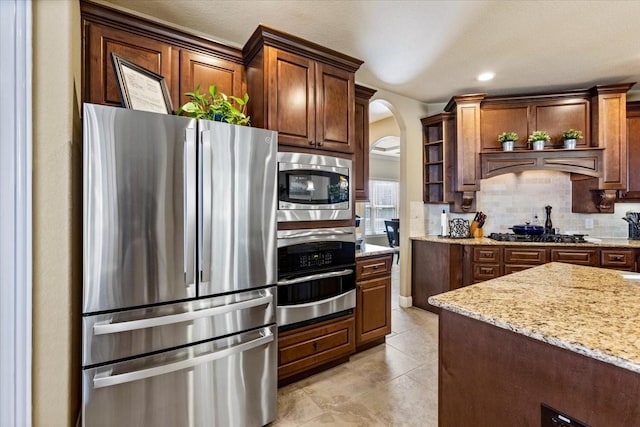 kitchen with backsplash, light tile patterned flooring, light stone counters, and stainless steel appliances