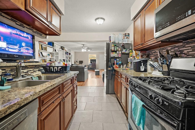 kitchen with ceiling fan, sink, light stone countertops, light tile patterned floors, and appliances with stainless steel finishes