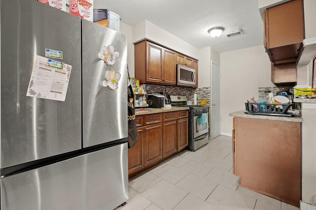 kitchen with a textured ceiling, light tile patterned floors, backsplash, and appliances with stainless steel finishes