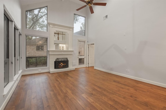 unfurnished living room featuring hardwood / wood-style floors, a high ceiling, and a brick fireplace