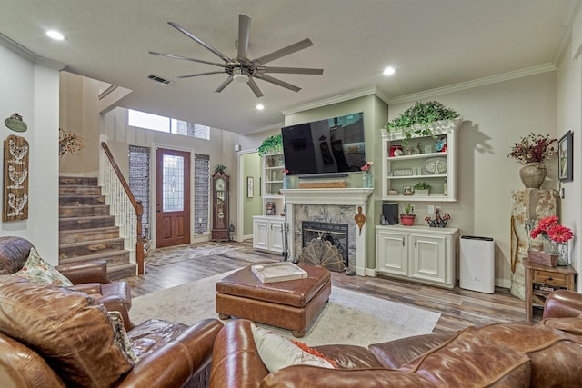 living room featuring a tiled fireplace, crown molding, ceiling fan, and light hardwood / wood-style floors