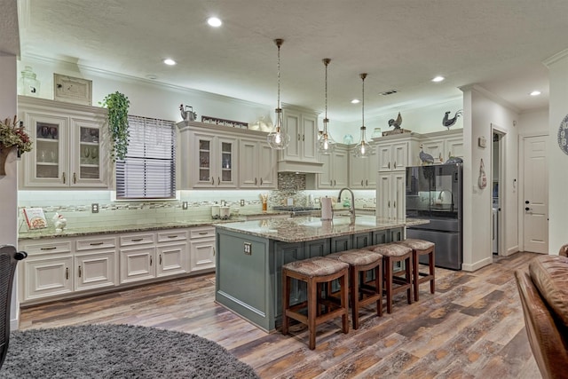 kitchen featuring hanging light fixtures, light stone counters, a kitchen bar, black refrigerator, and a center island with sink