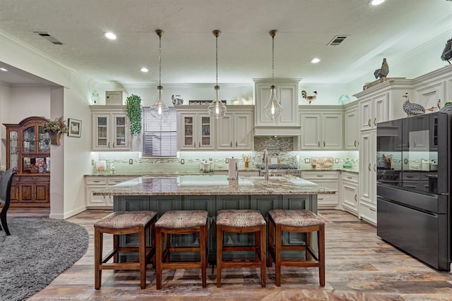 kitchen with black refrigerator, pendant lighting, light stone countertops, and a kitchen island with sink