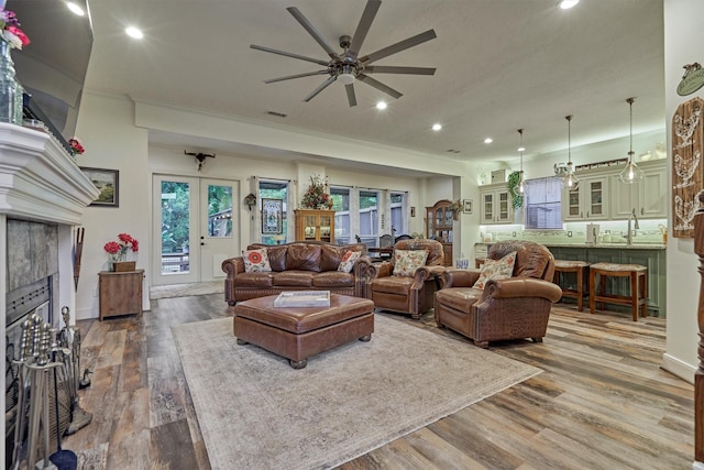 living room featuring french doors, hardwood / wood-style flooring, ceiling fan, a wealth of natural light, and a tiled fireplace