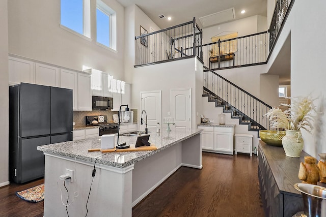 kitchen with black appliances, light stone countertops, white cabinets, and a towering ceiling