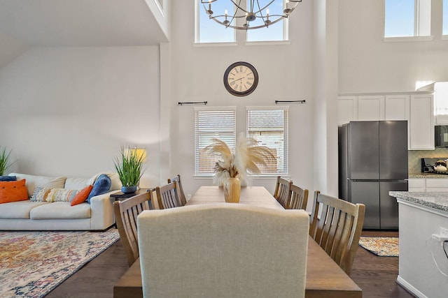 dining space with plenty of natural light, a towering ceiling, dark wood-type flooring, and an inviting chandelier