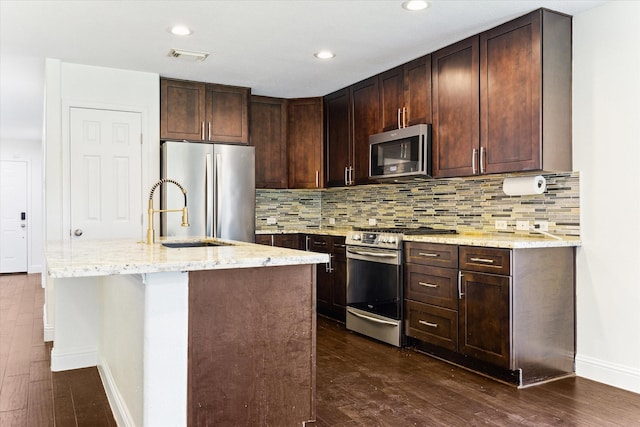 kitchen with appliances with stainless steel finishes, backsplash, a kitchen island with sink, sink, and dark hardwood / wood-style floors