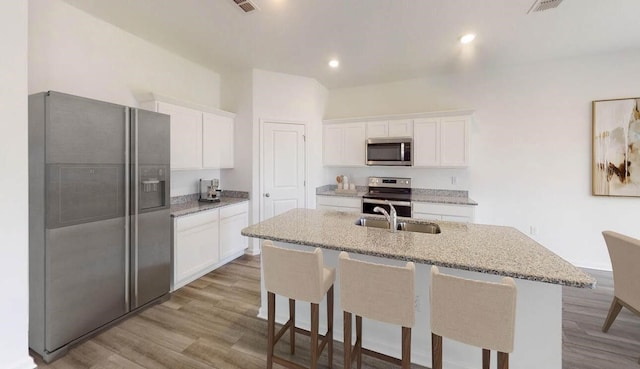 kitchen featuring white cabinetry, sink, stainless steel appliances, a breakfast bar, and a center island with sink