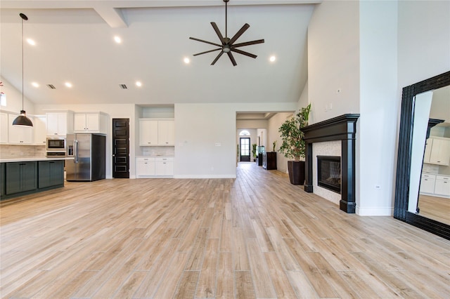 unfurnished living room with beam ceiling, ceiling fan, a towering ceiling, and light wood-type flooring