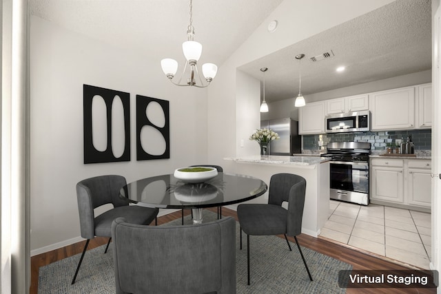 dining space with a textured ceiling, a chandelier, vaulted ceiling, and light hardwood / wood-style floors