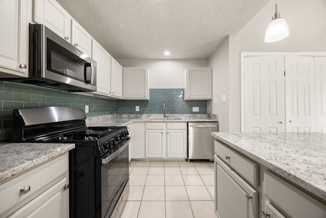 kitchen with stainless steel appliances, sink, light tile patterned floors, white cabinetry, and hanging light fixtures