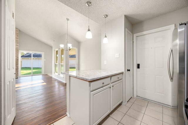 kitchen featuring stainless steel refrigerator, hanging light fixtures, white cabinets, vaulted ceiling, and light tile patterned floors