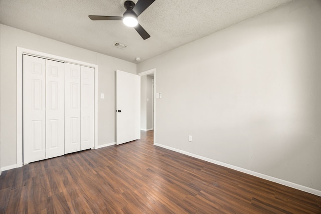 unfurnished bedroom with a textured ceiling, ceiling fan, dark wood-type flooring, and a closet