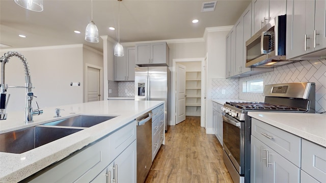 kitchen with appliances with stainless steel finishes, gray cabinetry, crown molding, sink, and hanging light fixtures