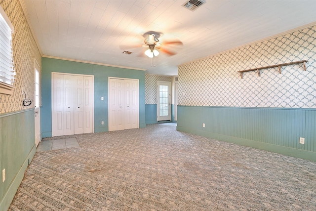 unfurnished bedroom featuring multiple closets, ceiling fan, crown molding, and carpet floors