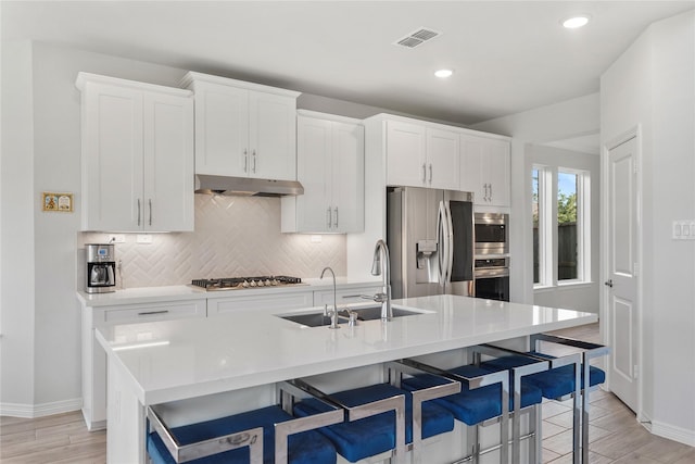 kitchen featuring a center island with sink, a kitchen breakfast bar, white cabinets, sink, and appliances with stainless steel finishes