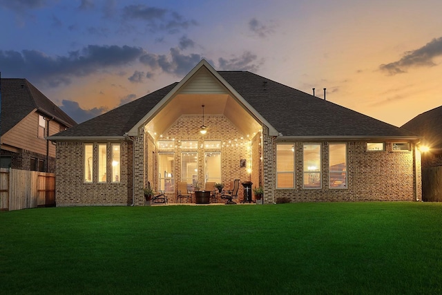 back house at dusk with a patio and a lawn